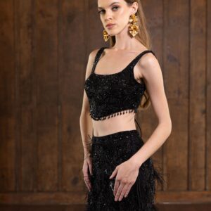 The model is wearing a black Alinia gown with feathers and a crop top.