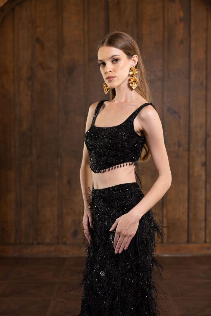 The model is wearing a black Alinia gown with feathers and a crop top.