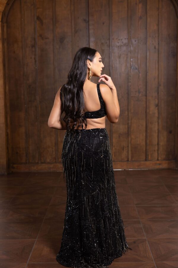 A woman in a black sequined Victoria dress posing in front of a wooden wall.