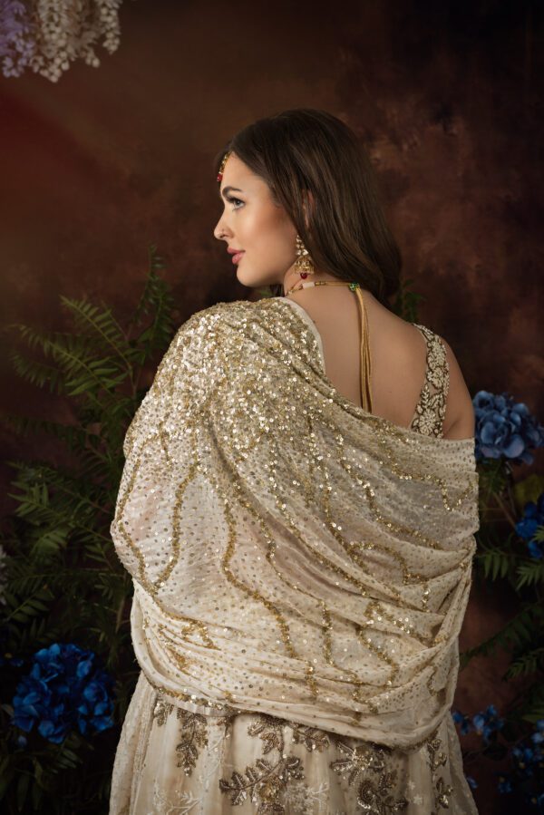 The back view of a woman in a white and gold PERLA lehenga.