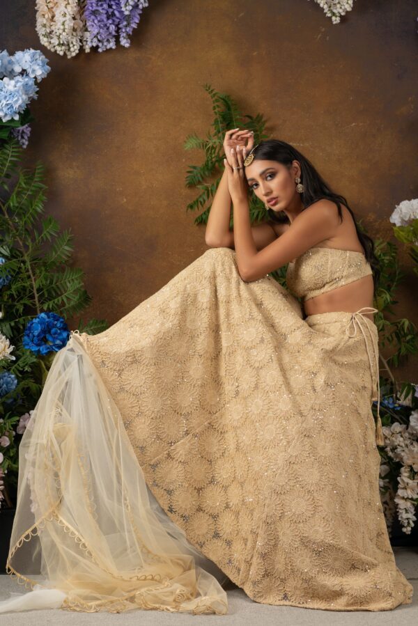 A Vikaya in a beige lehenga posing in front of flowers.