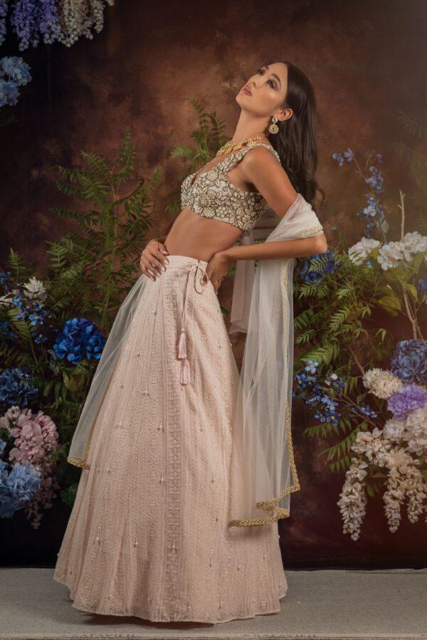 A model in a pink Niaa lehenga posing in front of flowers.