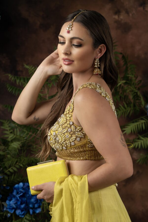 A woman in a yellow lehenga posing with a Miraya clutch.